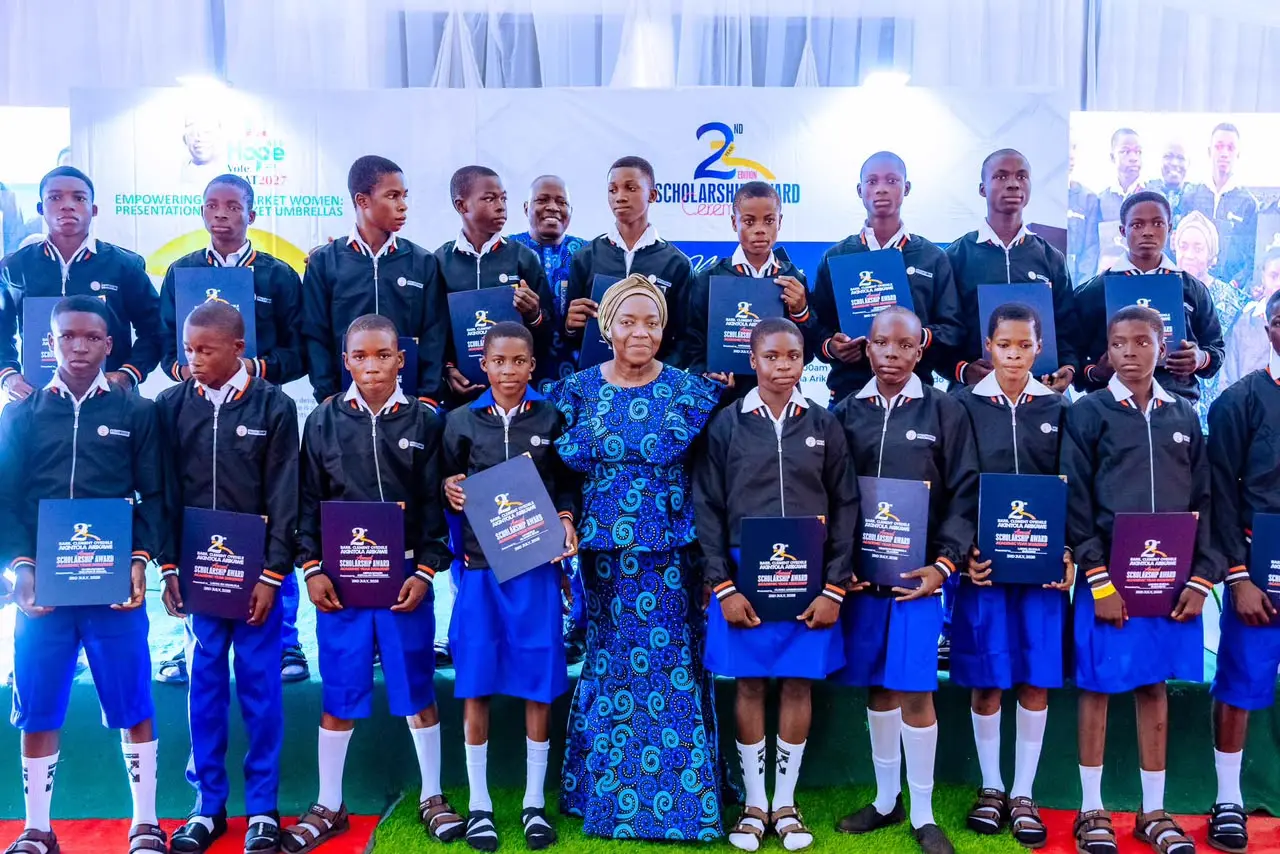 A collective triumph: High school scholarship winners hold up their academic excellence folders on stage alongside family representatives.